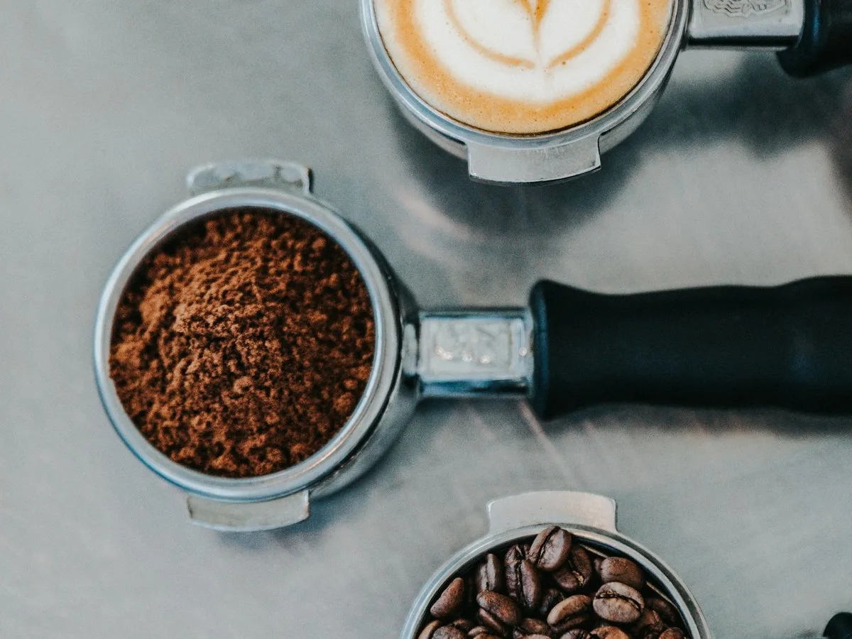 Three portafilters in a row: whole beans, ground coffee and the finished cup with milk foam